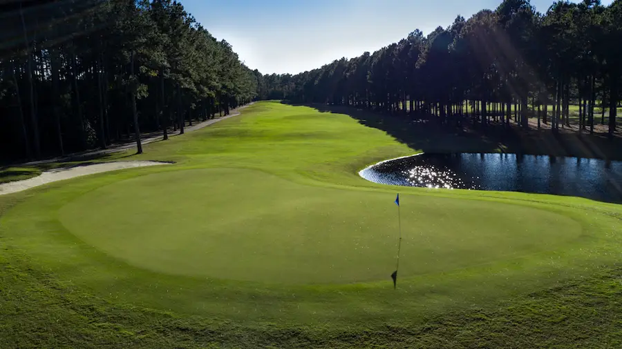View down a fairway at Crown Park Golf Club with a pond on the right and tall pines lining both sides