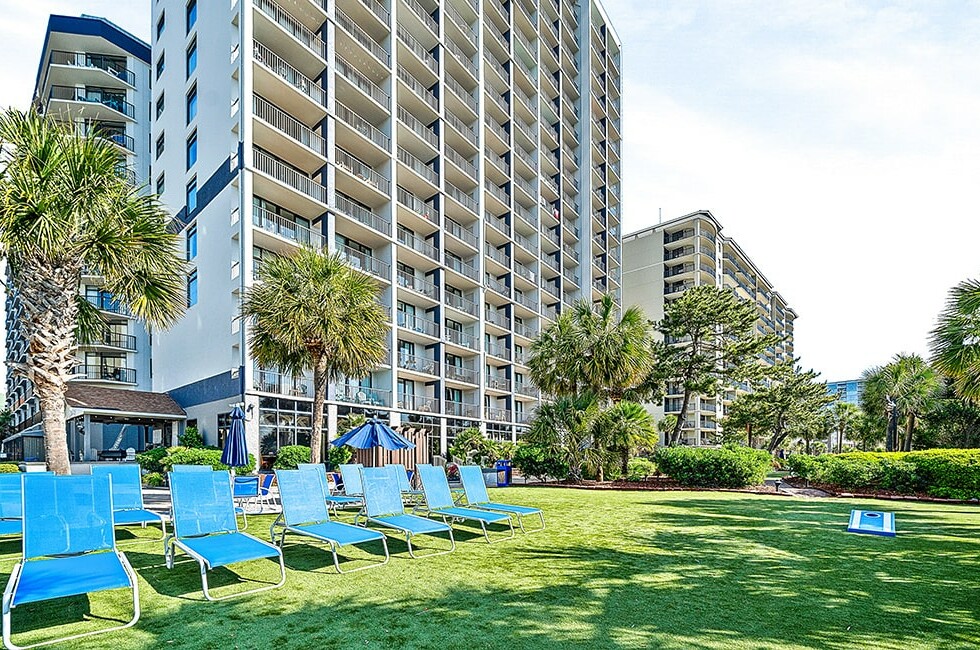 The oceanfront towers at Beach Colony Resort seen across the lawn and sun loungers