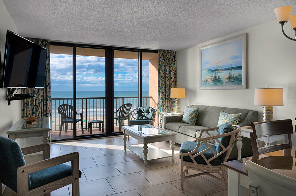 Living area of an oceanfront condo at Beach Colony Resort, looking out to the balcony and the water
